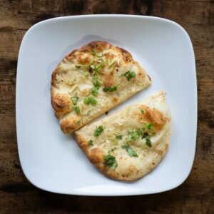 Appetizing garlic naan bread on a white plate, garnished with herbs.