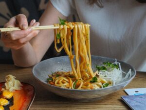 NOODLES(1plate) Close-up of a person using chopsticks to enjoy flavorful Asian noodles in a bowl.