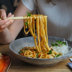 Close-up of a person using chopsticks to enjoy flavorful Asian noodles in a bowl.