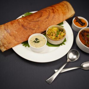Crispy dosa served with coconut chutney, vegetable curry, and sambar on a black background.