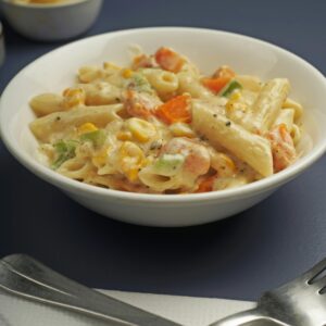 Delicious creamy penne pasta served with mixed vegetables on a dark table.